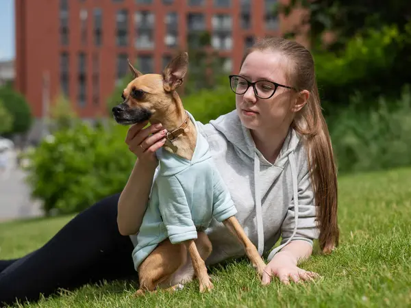 Küçük bir köpekle yürürken çimenlerde yatan beyaz bir kadın.