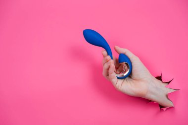 Mavi vibratörlü el pembe kağıt arkaplanından sarkıyor.