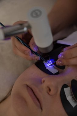 Kirpik uzatma prosedüründen geçen bir kadın ultraviyole lamba kullanıyor.