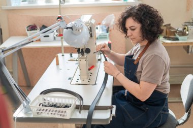 Bir kadın tabakçı dikiş makinesine deri kemer dikiyor.