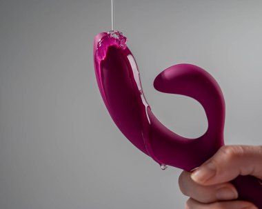 Lube pouring on pink dildo on white background
