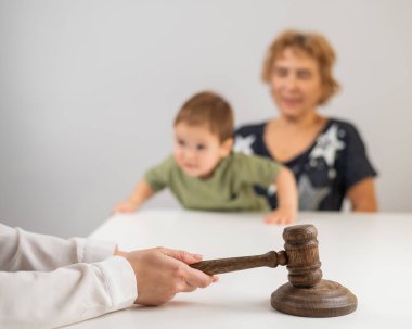 Hakim, elinde çocuk tutan yaşlı bir kadının arka planına vuruyor.