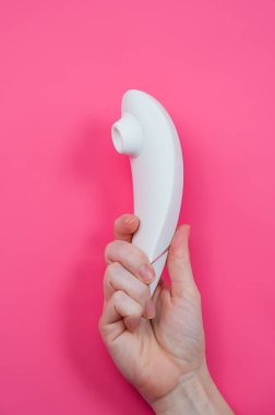 Pembe arka planda beyaz süpürge klitoral vibratör tutan kadın.