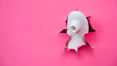 Beyaz vakumlu klitoral vibratör pembe kağıt arkaplanından sarkıyor. Seks oyuncağı