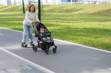 Beyaz kadın bebek arabasıyla küçük oğluyla paten kayıyor.