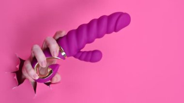 Kadın eli pembe kağıttan yapılmış pembe seks oyuncağıyla dışarıda duruyor.