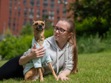 Küçük bir köpekle yürürken çimenlerde yatan beyaz bir kadın.