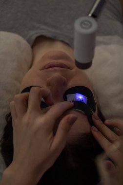 Bir usta, LED lamba kullanarak bir kadına kirpiklerini uzatır. Dikey fotoğraf