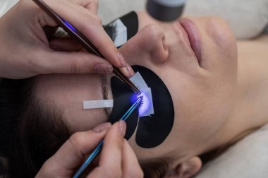 Kirpik uzatma prosedüründen geçen bir kadın ultraviyole lamba kullanıyor.