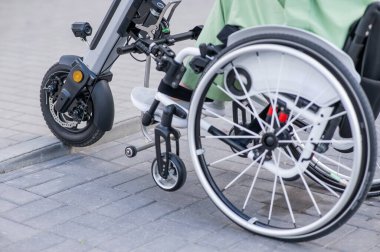 Tekerlekli sandalyedeki yüzü olmayan ve manuel kontrol için yardımcı bir aleti olan bir kadın. Elektrikli bisiklet.