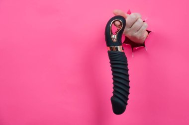 Siyah desenli vibratörlü, pembe kağıt arkaplanından çıkmış bir kadın eli. Boşluğu kopyala