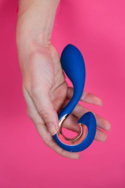 Pembe arka planda mavi vibratörlü bir el. Dikey fotoğraf