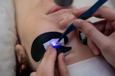 Kirpik uzatma prosedüründen geçen bir kadın ultraviyole lamba kullanıyor.