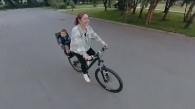 Beyaz kadın oğlunu bisiklet koltuğunda taşıyor.