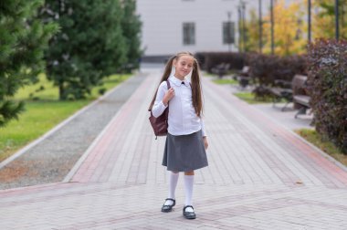Beyaz üniformalı ve sırt çantalı bir kız okuldan ayrılıyor.