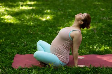 Hamile beyaz kadın parkta yoga yapıyor.