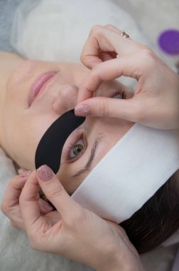 Efendi, LED kirpik uzantılarından önce ultraviyole ışınlara izin vermeyen koruyucu yamalar uyguluyor. Dikey fotoğraf