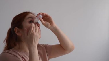 Beyaz kadın gözlerine nemlendirici damlalar sürüyor.