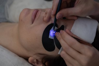 Kirpik uzatma prosedüründen geçen bir kadın ultraviyole lamba kullanıyor.