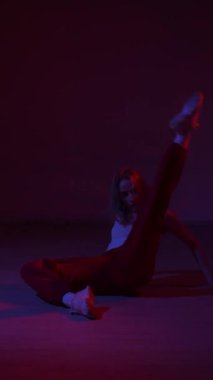 Genç bir kadın mavi ve kırmızı ışıkta çağdaş dans ediyor. Dikey video