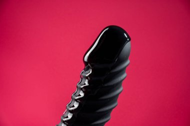 Lube pouring on black dildo on pink background