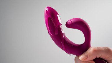 Lube pouring on pink dildo on white background