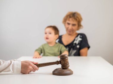 Hakim, elinde çocuk tutan yaşlı bir kadının arka planına vuruyor.