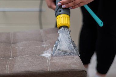 Kadın, elektrikli süpürge ve fırça kullanarak kumaş sandalyesini temizliyor.