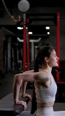 Beyaz kadın spor salonundaki bankta şınav çekiyor.