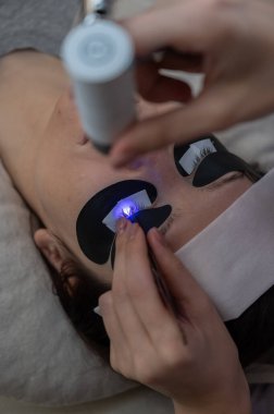 Kirpik uzatma prosedüründen geçen bir kadın ultraviyole lamba kullanıyor.