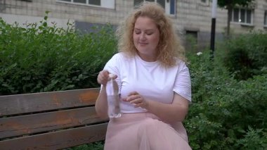 Fazla kilolu beyaz kadın yürürken su içer.