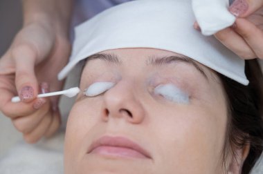 Usta, müşterilere pamuk çubuğu kullanarak kirpiklerini temizleme köpüğü sürüyor.