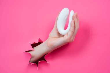 Beyaz bir seks oyuncağıyla pembe bir arka planda duran bir kadın eli.