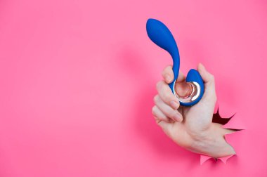 Mavi vibratörlü el pembe kağıt arkaplanından sarkıyor.