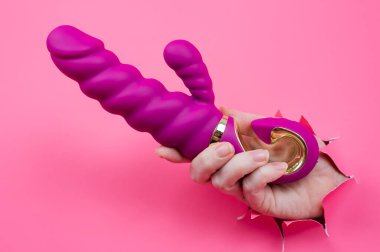 Kadın eli pembe kağıttan yapılmış pembe seks oyuncağıyla dışarıda duruyor.