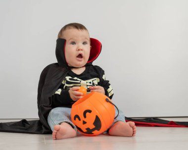Beyaz arka planda şeker sepeti tutan Dracula Cadılar Bayramı kostümlü beyaz tatlı çocuk.
