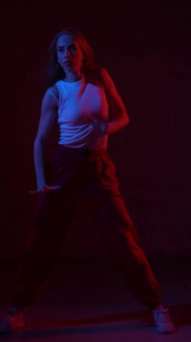 Genç bir kadın mavi ve kırmızı ışıkta çağdaş dans ediyor. Dikey video