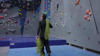 Beyaz bir adam tırmanma duvarındaki bir derste güvenlik ipi tutuyor.