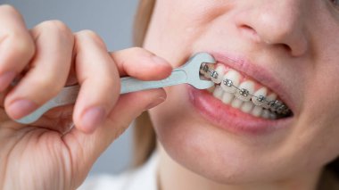 Kadın şaka gibi bir İngiliz anahtarıyla frenlerin kablosunu sıkıyor. Isırık düzeltme aygıtı.