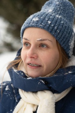 Dişlerinde diş teli olan beyaz bir kadın kışın dışarıda yürüyor.