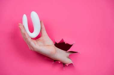 Beyaz bir seks oyuncağıyla pembe bir arka planda duran bir kadın eli.