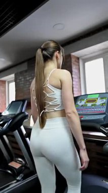 Beyaz kadın spor salonunda koşu bandında yürüyor.