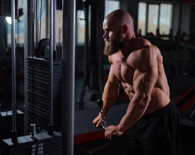 Kel Kafkas vücut geliştirici kabloyla ağır triseps egzersizleri yapıyor.