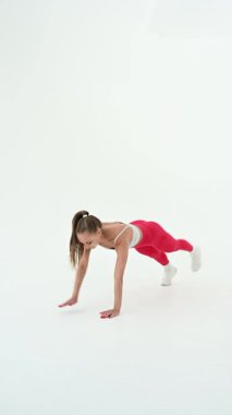 Genç bir kadın beyaz arka planda kalas egzersizi yapıyor.