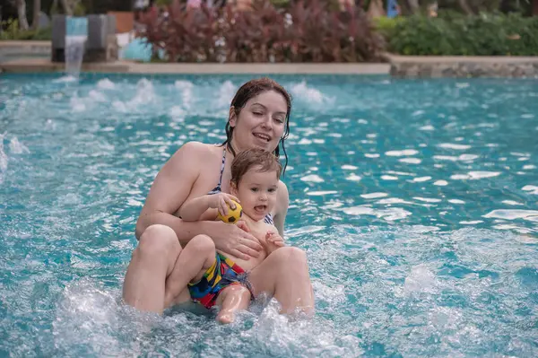 Beyaz bir kadın ve bir yaşındaki oğlu havuzda yüzüyorlar.