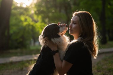 Beyaz bir kadın parkta yürürken köpeğine sarılıyor.