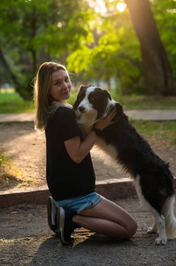 Beyaz bir kadın parkta yürürken köpeğine sarılıyor.