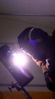 Koruyucu maske takan bir adam metal bir boruya kaynak yapar. Yavaş çekim