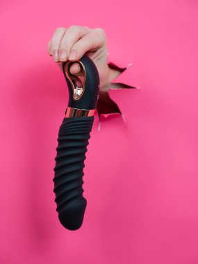 Siyah desenli vibratörlü, pembe kağıt arkaplanından çıkmış bir kadın eli. Dikey fotoğraf