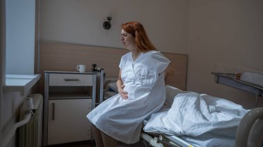 Mutsuz bir kadın kanepeye oturur ve doğum yaptıktan sonra karnını bir hastane odasında tutar.